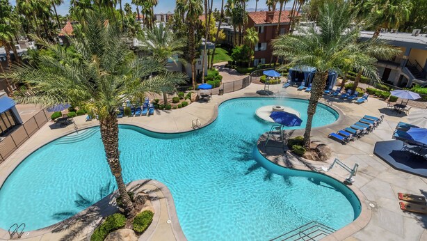A large, clear swimming pool with multiple lounge areas and palm trees. - Alexis Park All Suite Resort (Las Vegas)