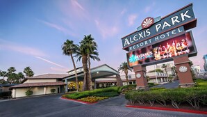 The exterior of the Alexis Park Resort Hotel with a prominent sign, palm trees, and well-maintained landscaping. - Alexis Park All Suite Resort (Las Vegas)