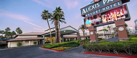 Das Äußere des Alexis Park Resort Hotels mit auffälliger Beschilderung, Palmen und gepflegter Bepflanzung.