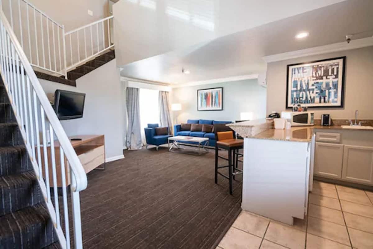 A modern apartment with a staircase, a living room with a blue sofa, a kitchen area, and a dining space.
