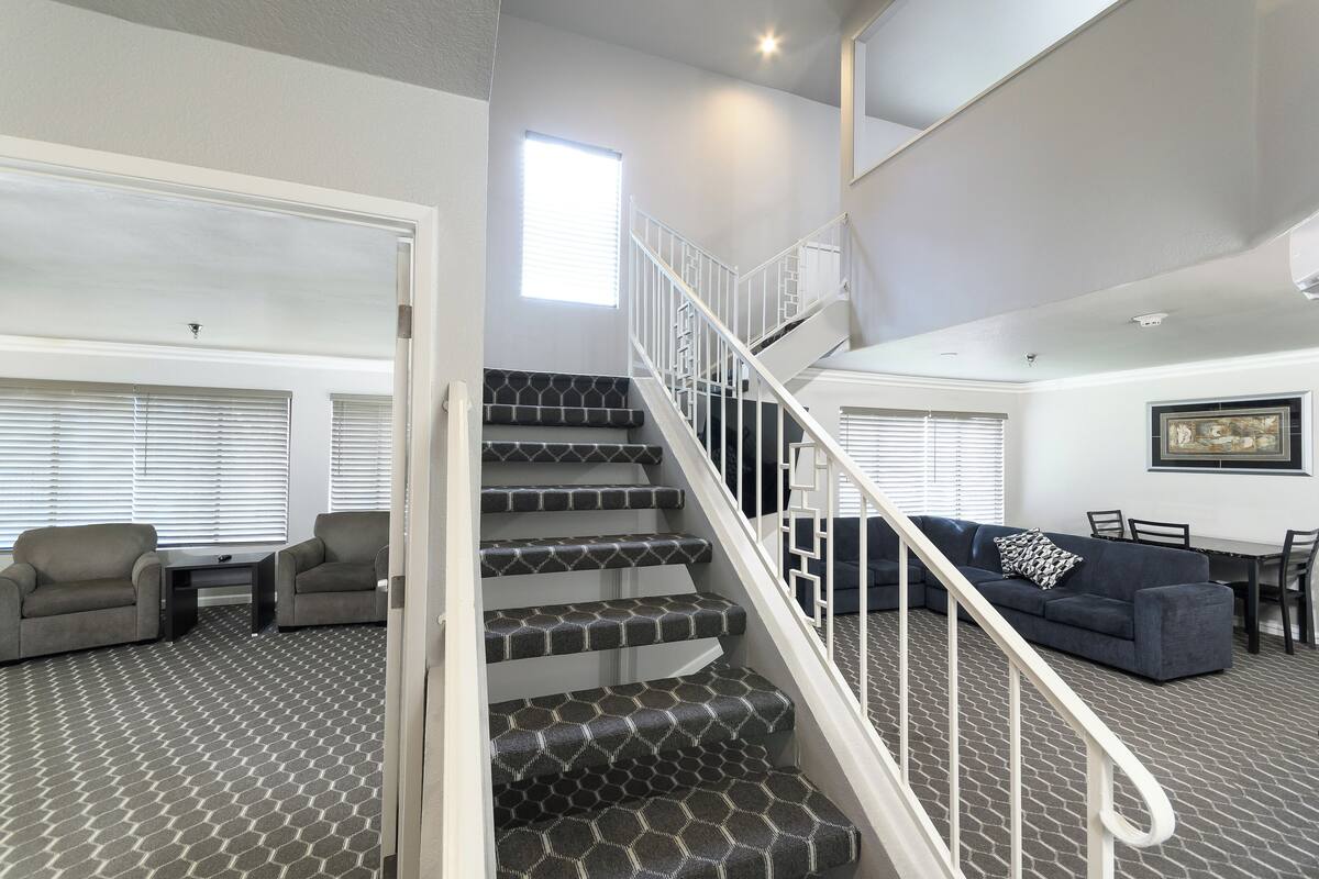A staircase with a white railing leading to a second floor. There are two gray armchairs and a dark gray sofa in the living area below.
