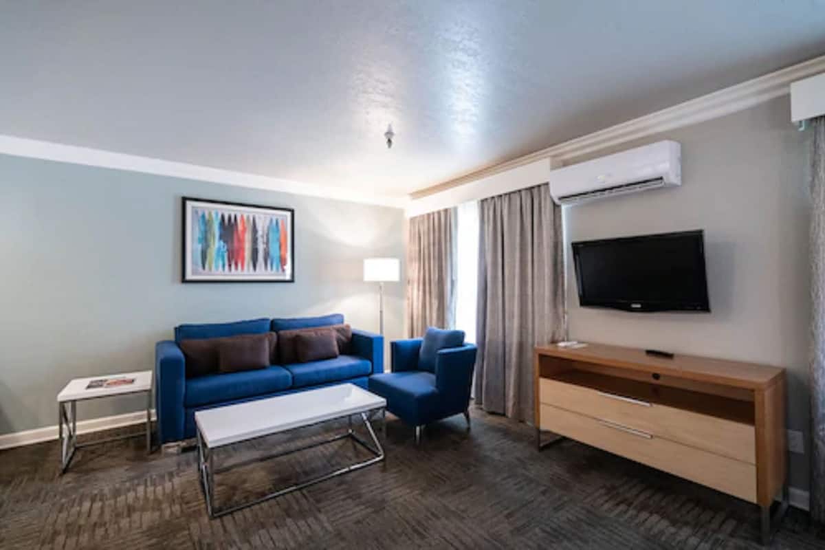 A modern hotel room with a blue sofa, a coffee table, a TV, and an air conditioning unit.