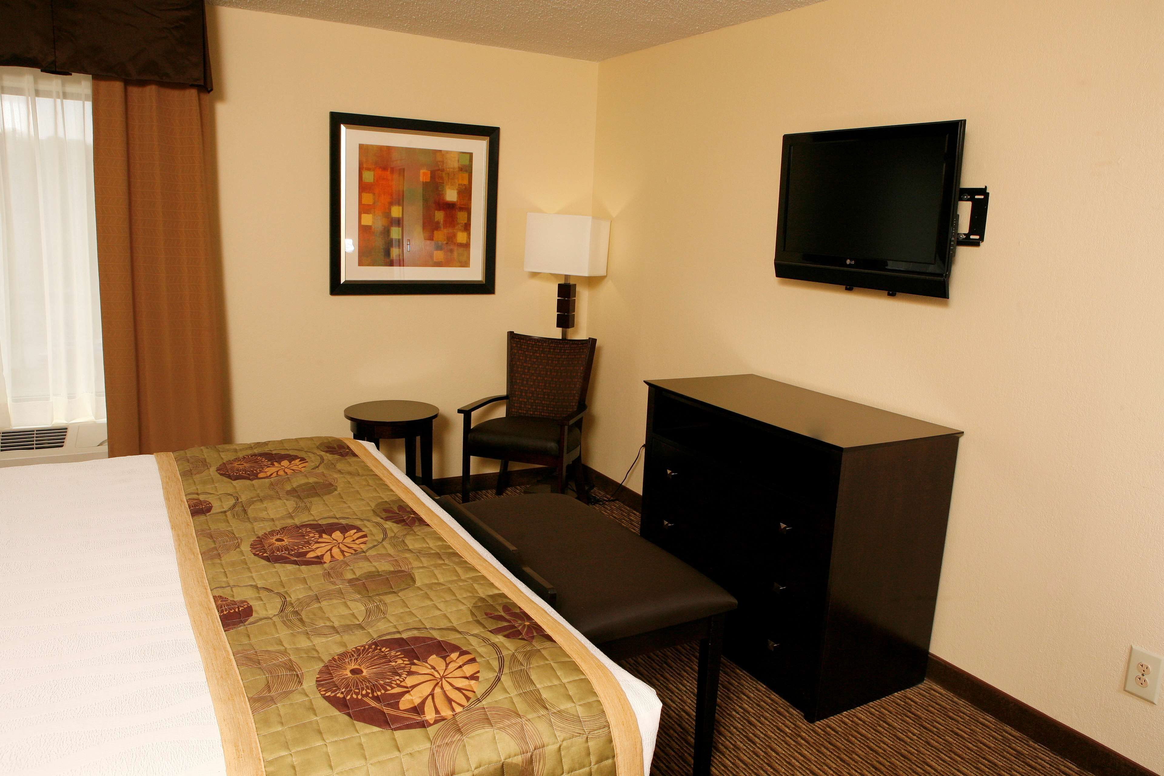 A hotel room with a bed, a desk with a chair, a television, and a framed picture on the wall.
