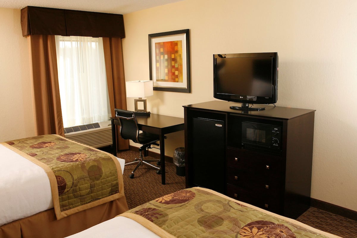 Habitación de hotel con dos camas, un escritorio con computadora, televisor y un cuadro en la pared.