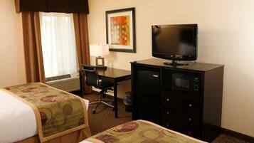 A hotel room with two beds, a desk with a computer, a television, and a framed picture on the wall.