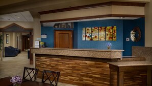 Zona de recepción con un mostrador de madera, pared azul con textura y una obra de arte floral enmarco.