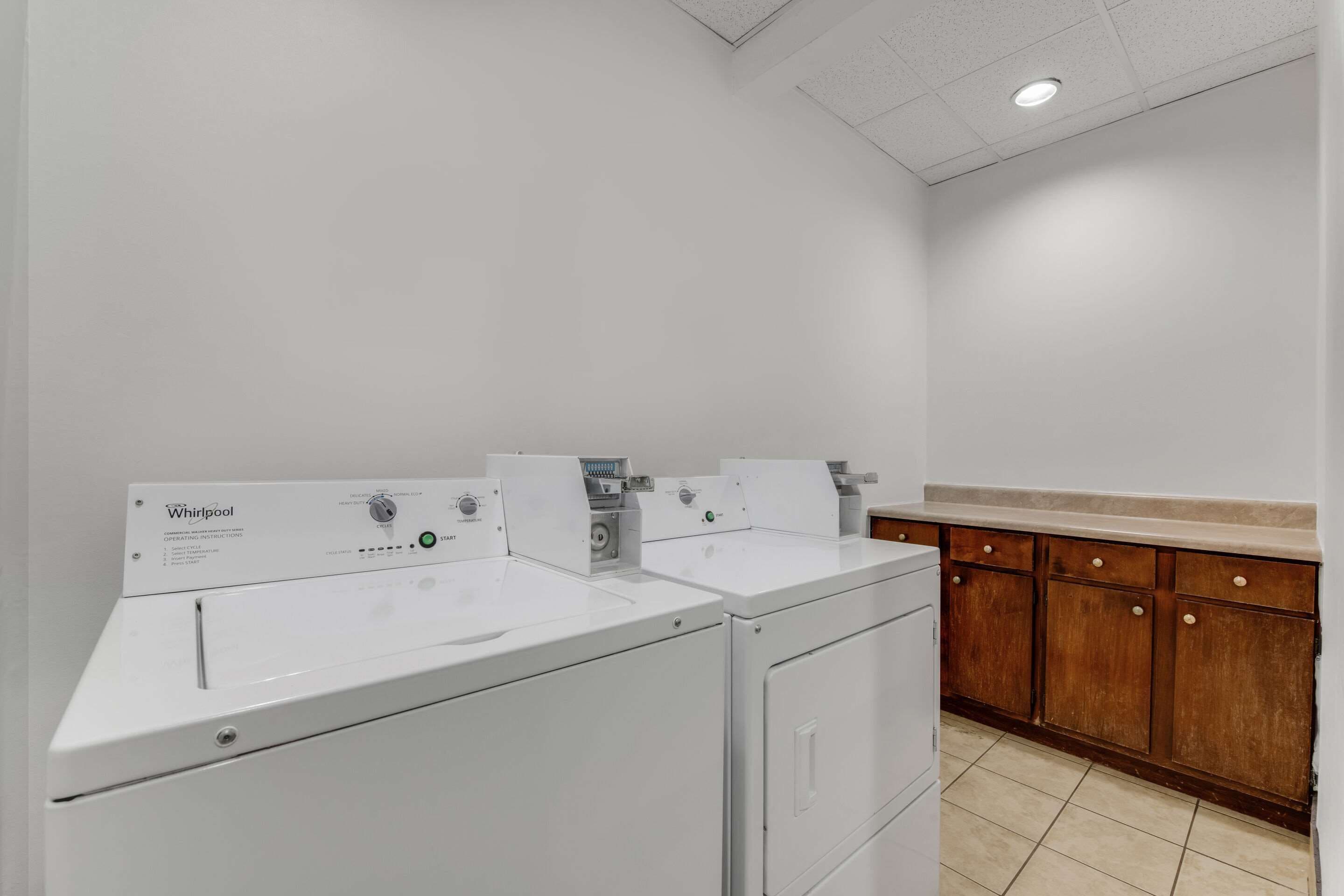 Une buanderie équipée de deux lave-linge Whirlpool et de meubles de rangement en bois.