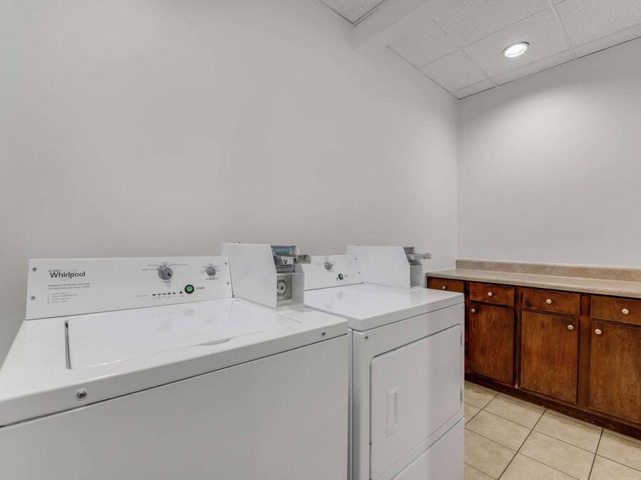 Une buanderie équipée de deux lave-linge Whirlpool et de meubles de rangement en bois.