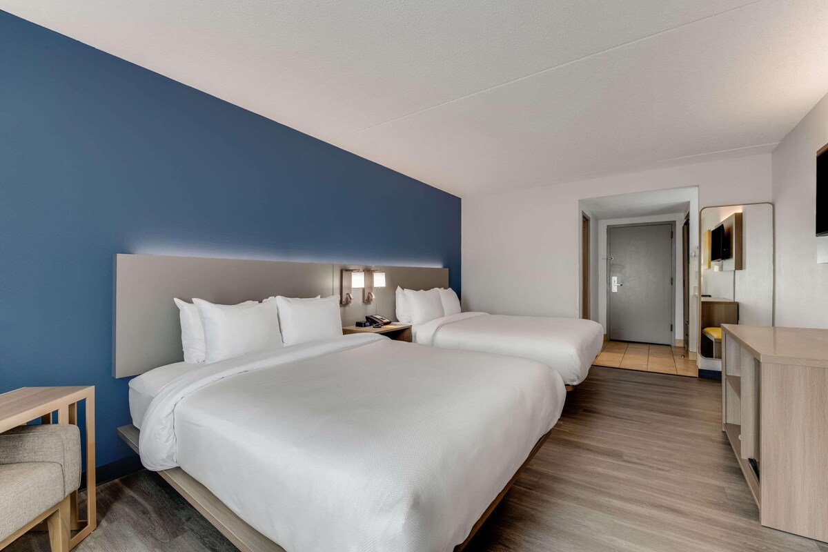 A hotel room with two beds, a desk, a chair, a TV, and a mirror.