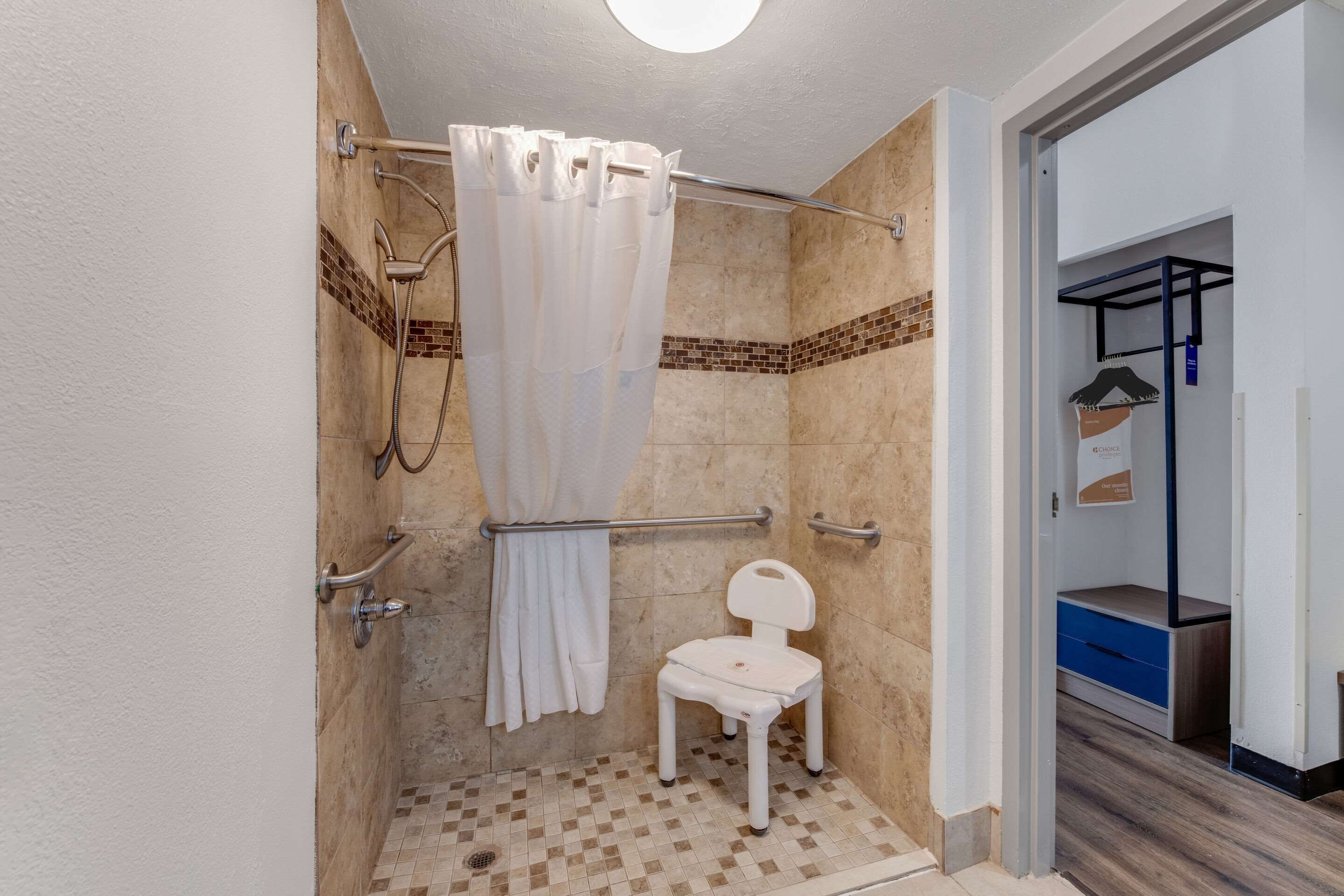 A shower area with a white shower chair, a shower curtain, and a grab bar.