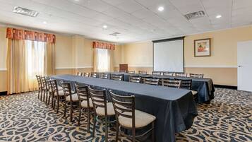 A conference room with a long table, chairs, a projector screen, and a carpeted floor.