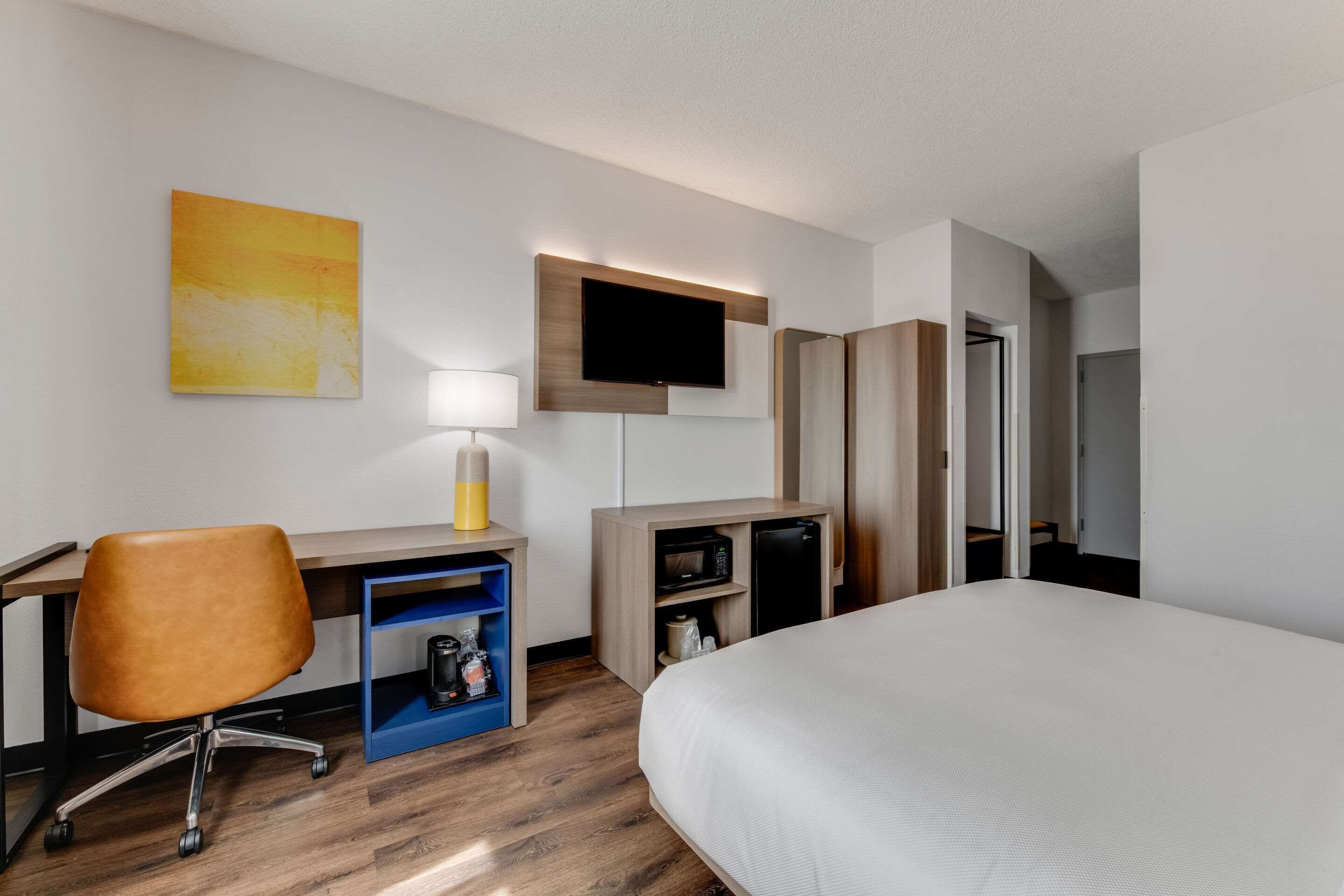 Una habitación de hotel con cama, escritorio, silla, televisor y una pequeña cocina.