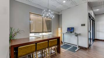 Un vestíbulo de hotel moderno con un mostrador de recepción de madera, un espejo grande, una araña y un monitor de computadora sobre una mesa blanca.