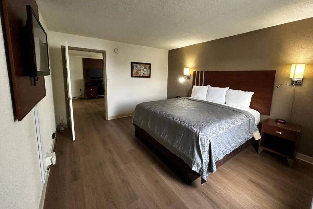 A hotel room with a bed, bedside lamps, a nightstand, a television, and a door leading to another room.