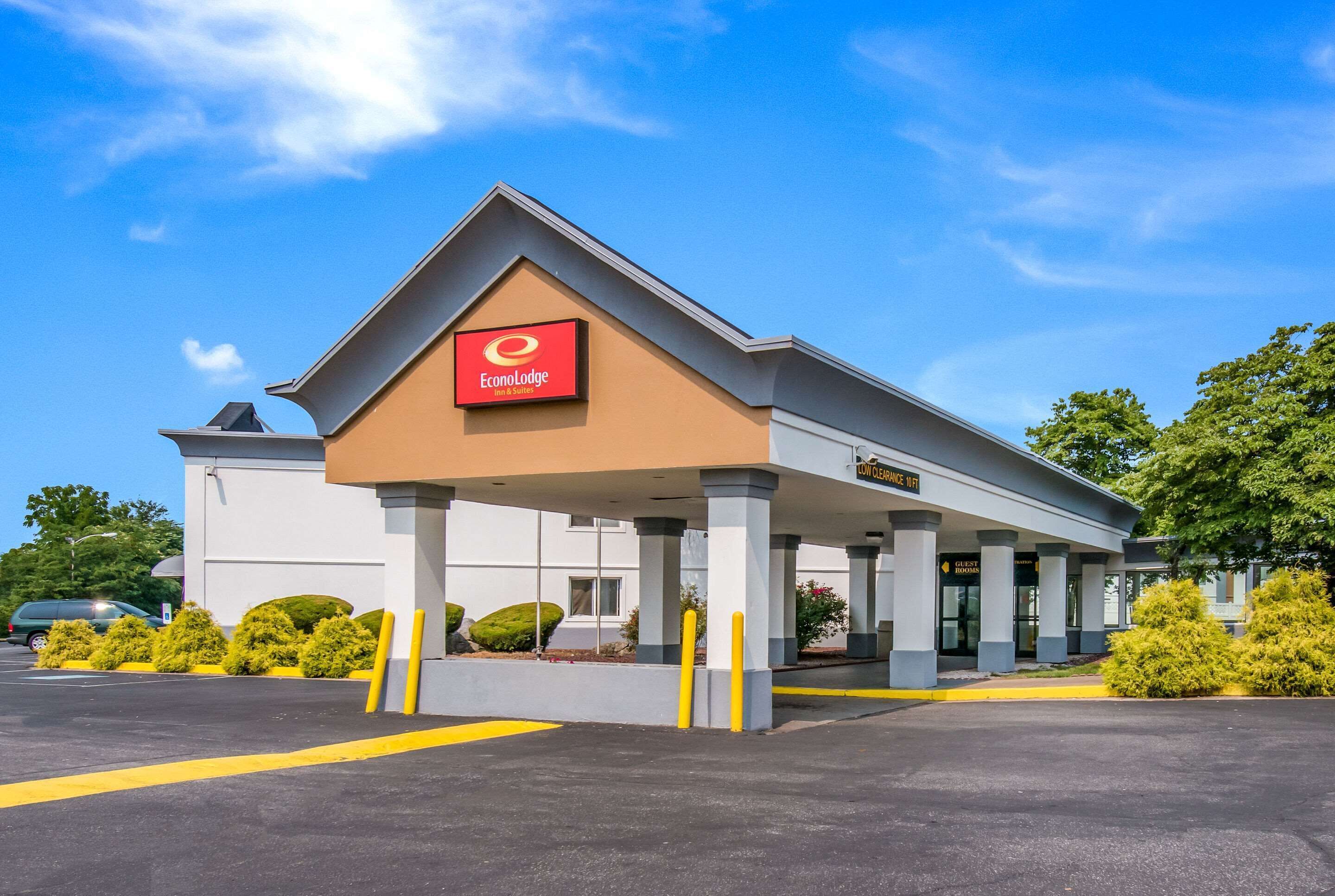 A hotel with a red and white sign, a covered entrance, and a parking lot.