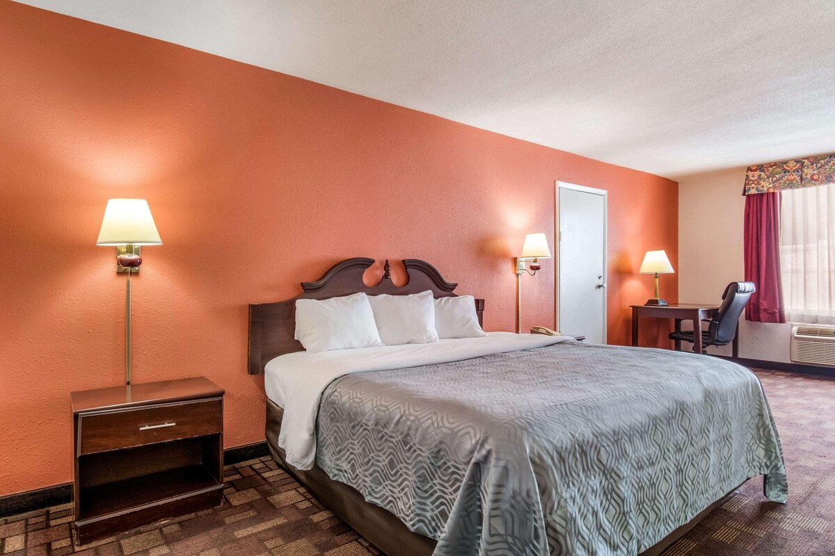 A hotel room with a bed, two bedside lamps, a desk, and a chair.