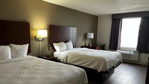 Habitación de hotel con dos camas, un escritorio, una silla, una lámpara y una ventana con cortinas.