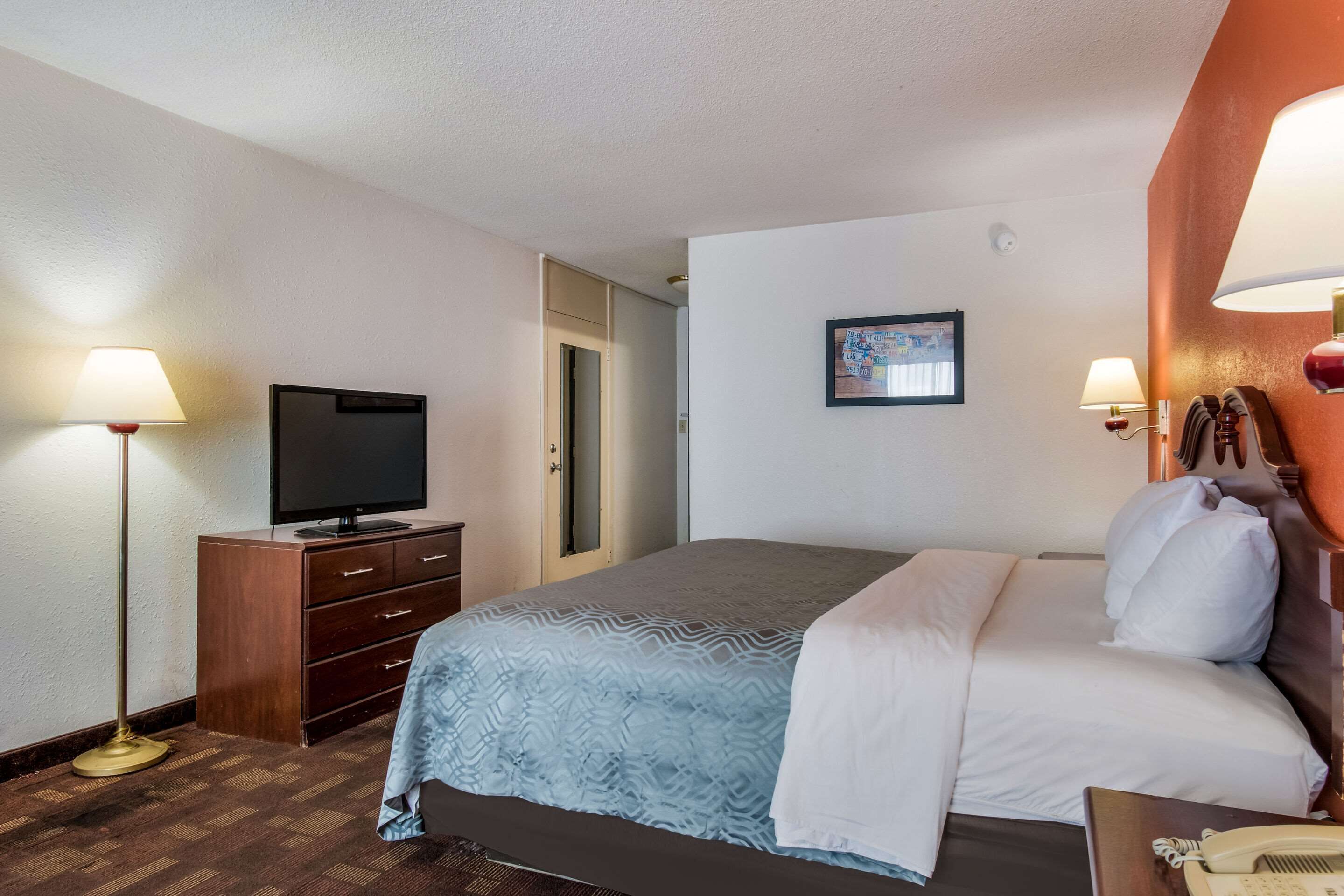 A hotel room with a bed, a TV, a desk with a telephone, and a lamp.