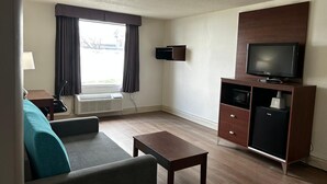 Una sala de estar compacta con sofá, mesa de centro, televisor sobre un mueble, calefactor y ventana con cortinas.