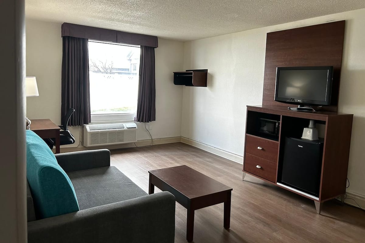 A compact living room with a sofa, a coffee table, a TV on a cabinet, a heater, and a window with curtains.