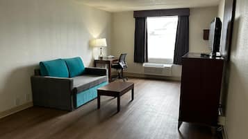 Une chambre d’hôtel équipée d’un canapé, d’une petite table, d’un bureau avec une chaise, d’un climatiseur et d’un téléviseur posé sur un meuble.