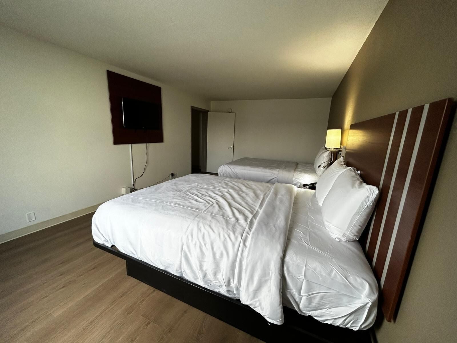 A hotel room with a large bed, a TV mounted on the wall, and a bedside table with a lamp.