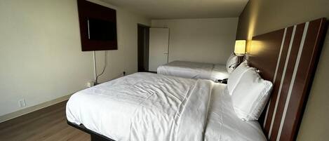 Habitación de hotel con una cama grande, un televisor montado en la pared y una mesita de noche con lámpara.