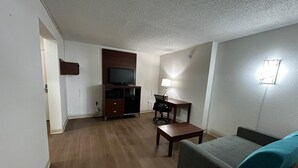 Una sala de estar con un televisor de pantalla plana, un escritorio con una lámpara y un sofá.