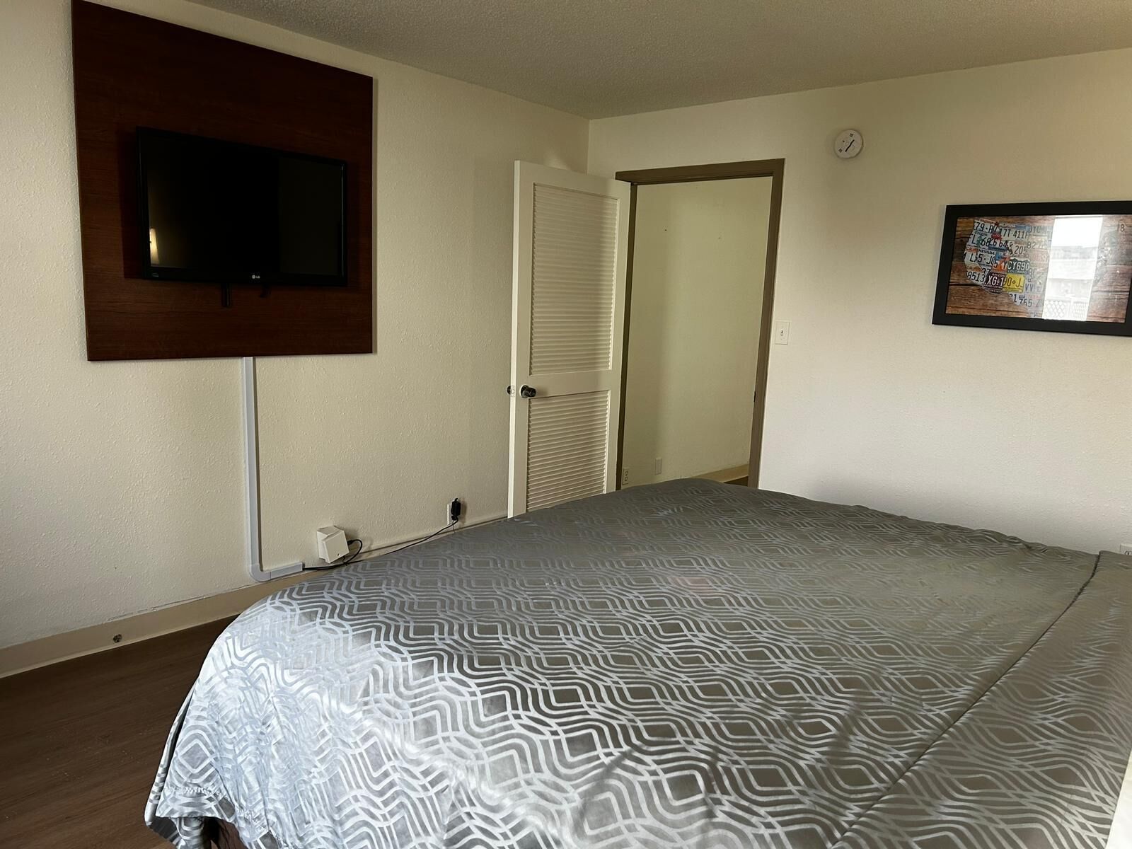 A bedroom with a bed, a television mounted on the wall, a door, and a framed picture on the wall.
