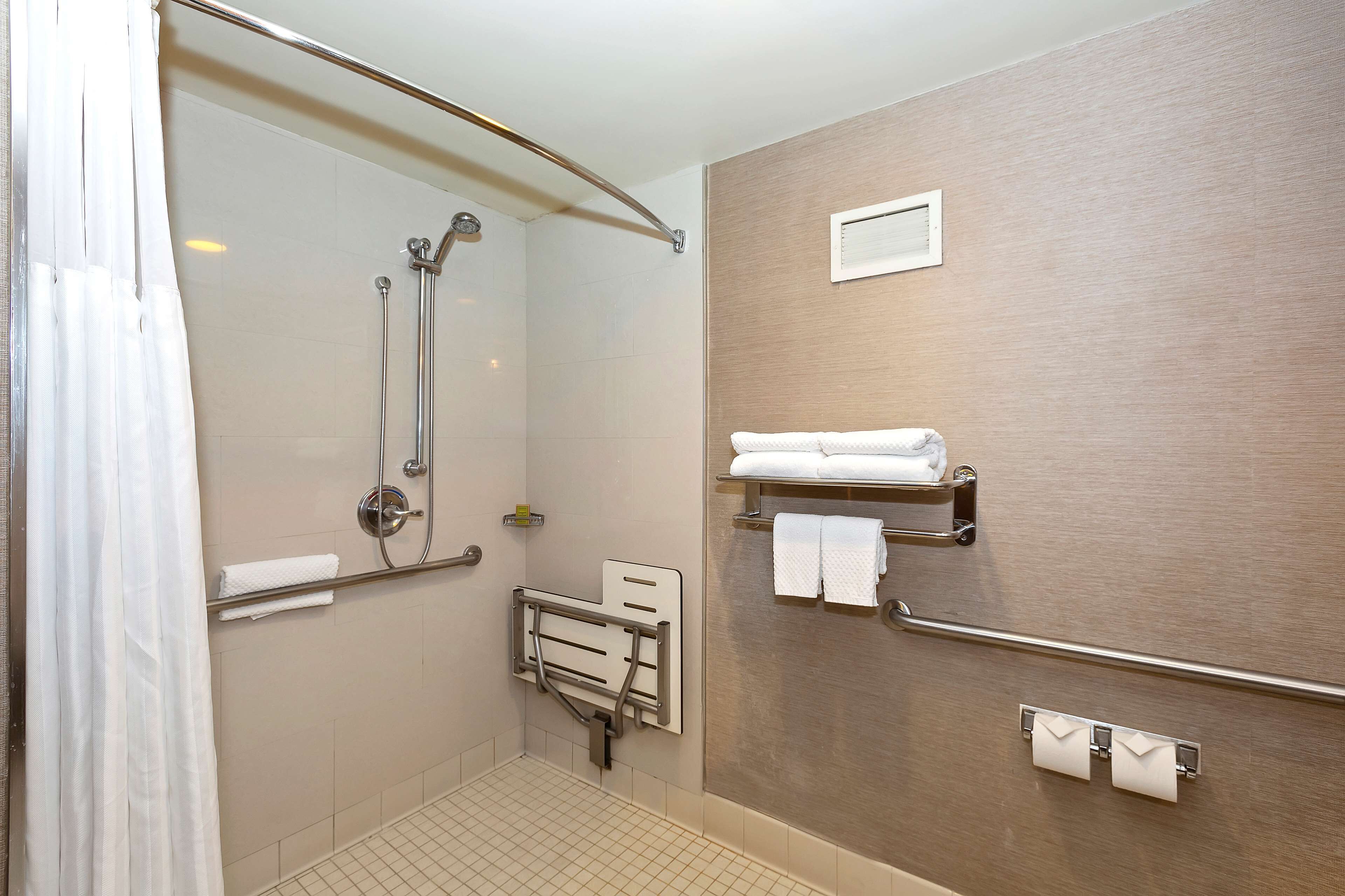 A modern bathroom with a shower, grab bars, a towel rack, and a toilet paper holder.