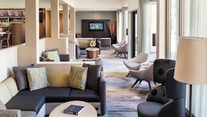 Un moderno vestíbulo de hotel con un sofá, sillones, una barra de café y un televisor.