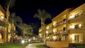 Un hotel de varios pisos con balcones, palmeras y un camino bien iluminado.