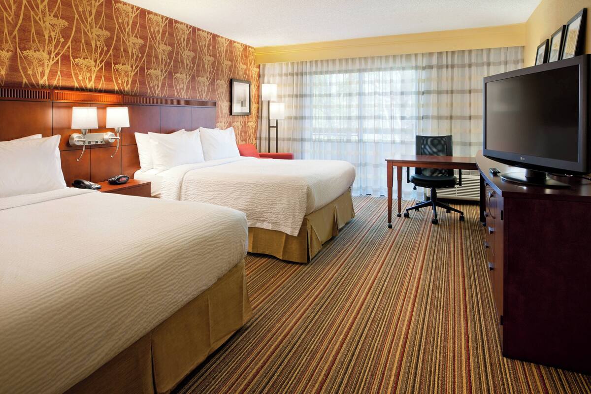 A hotel room with two beds, a television, a desk, and a chair.