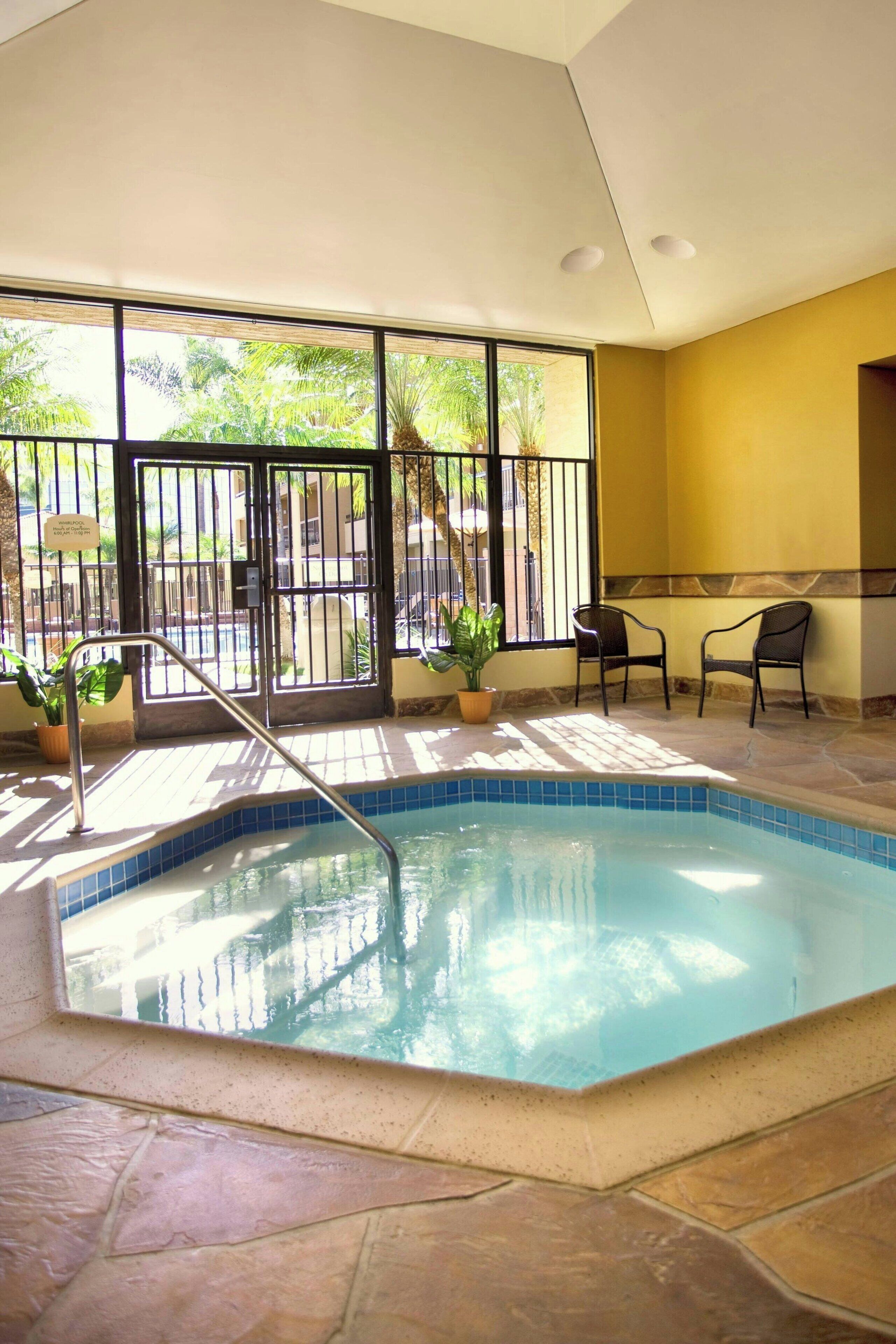 An indoor swimming pool with a tiled floor, a metal ladder, and two chairs near the pool.