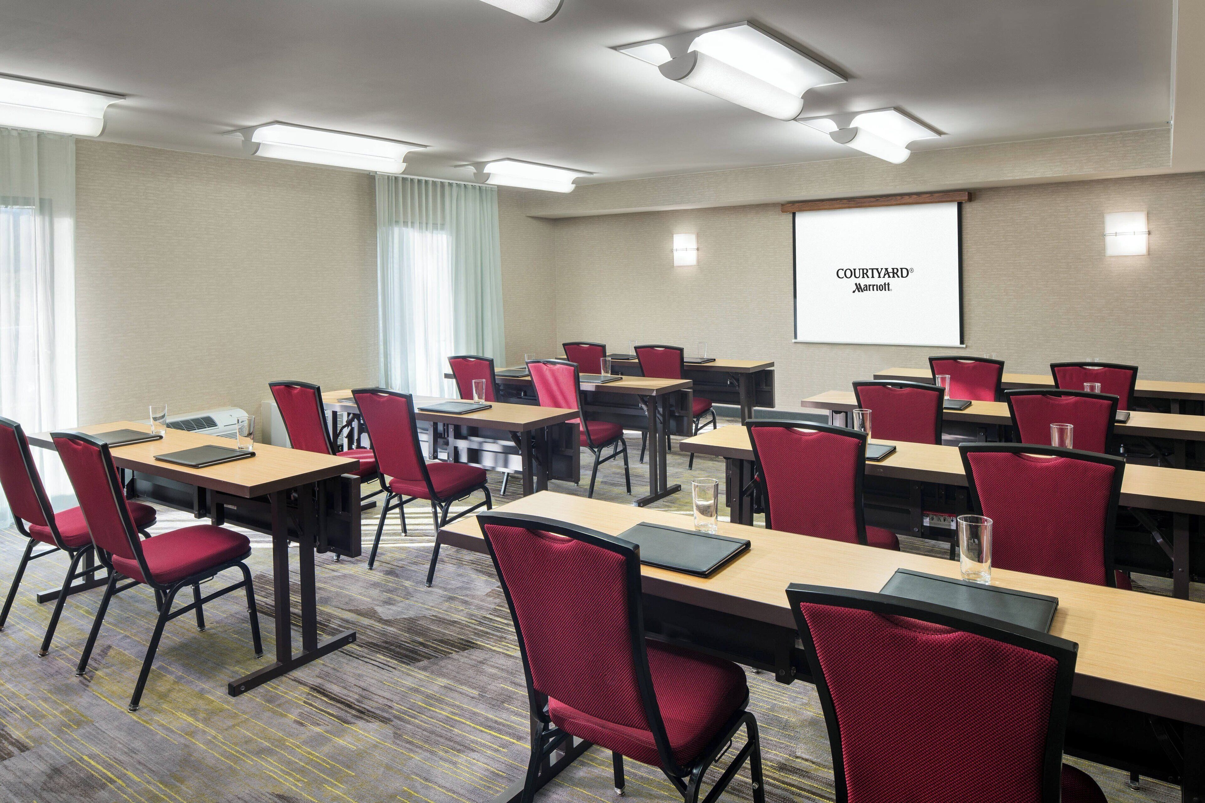 A conference room with multiple tables and chairs, a projector screen displaying 'Courtyard Marriott', and a carpeted floor.