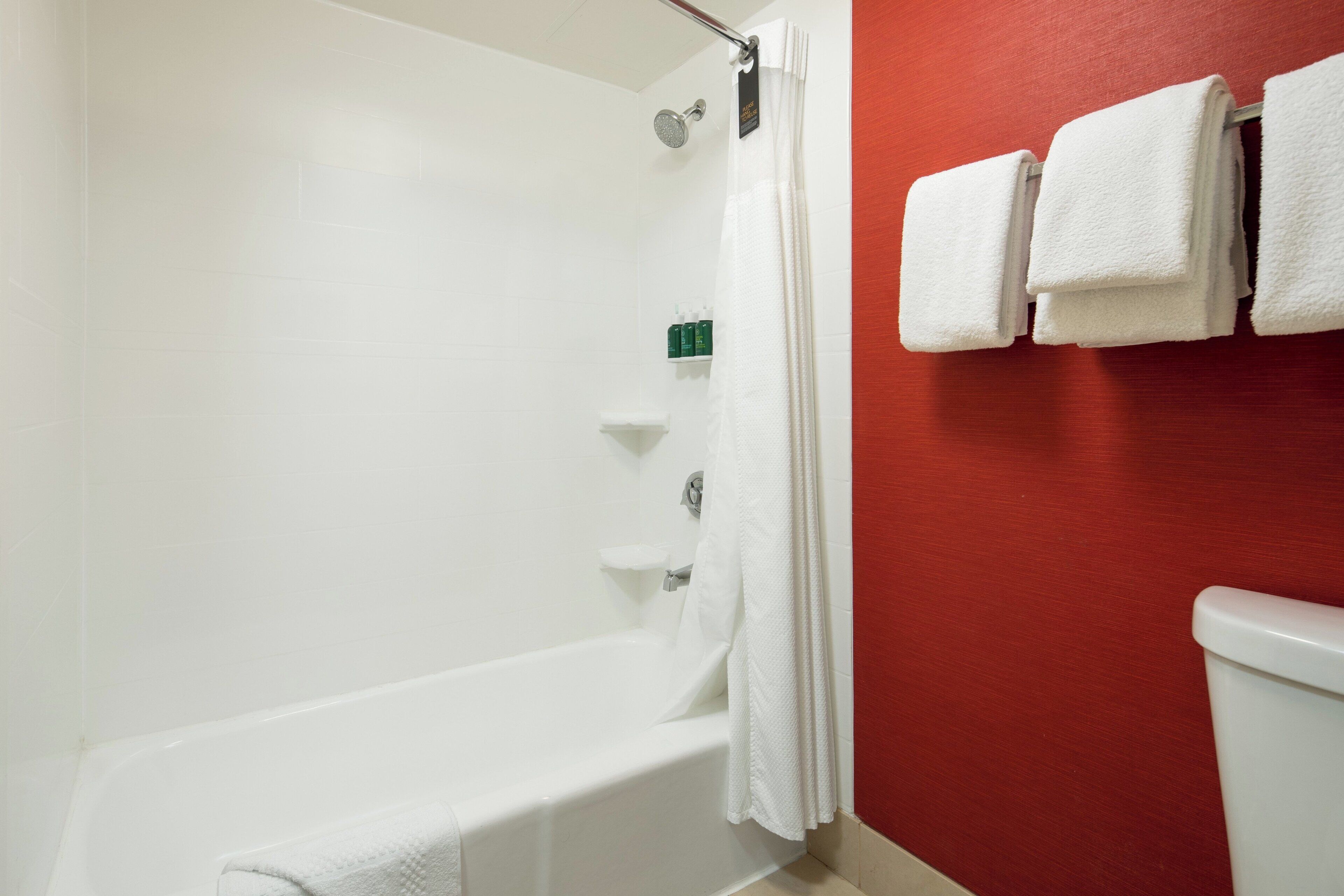 A bathroom with a white bathtub, a shower curtain, and a toilet. There are towels hanging on the wall.