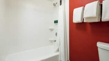 A bathroom with a white bathtub, a shower curtain, and a toilet. There are towels hanging on the wall.