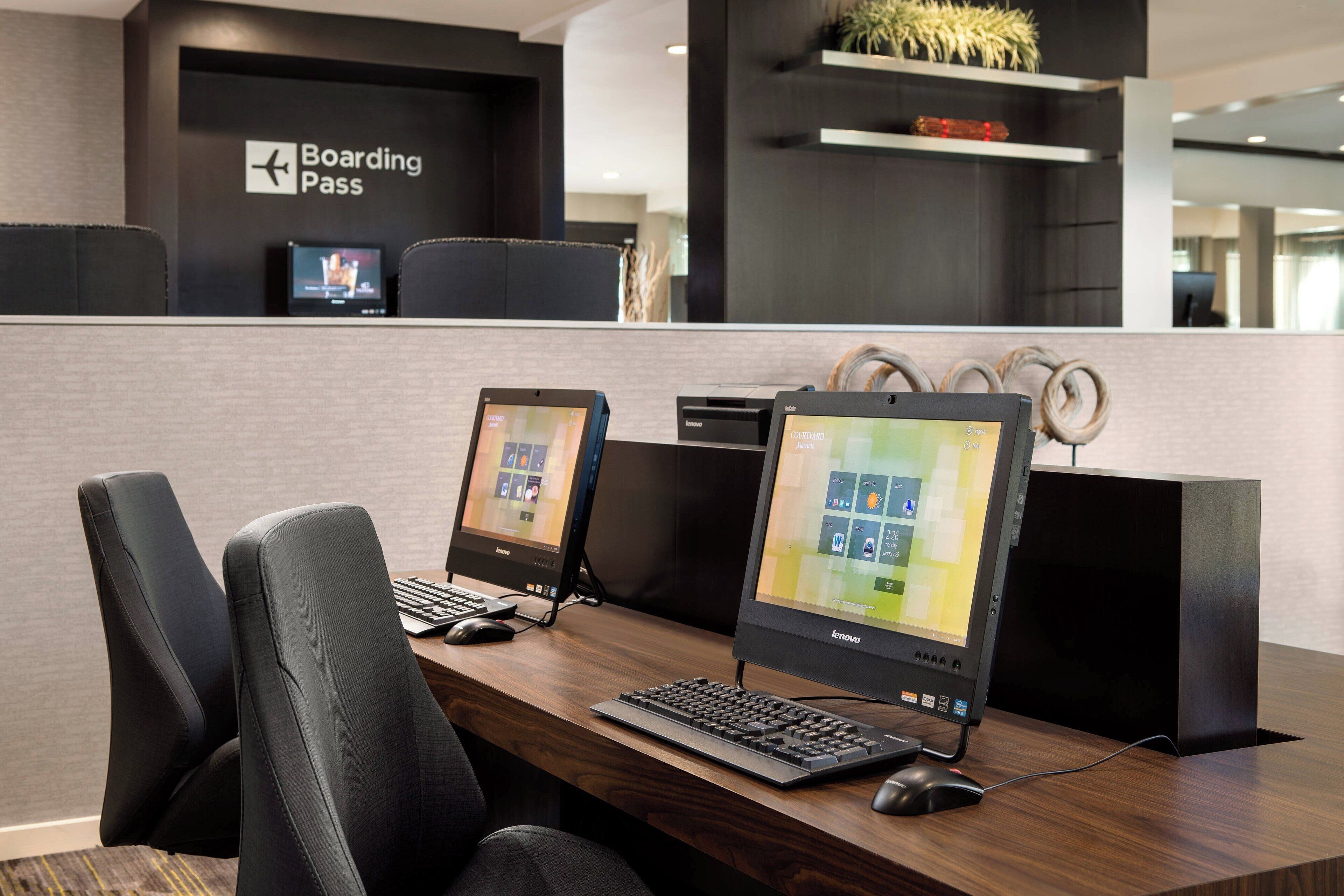 Un mostrador de registro con un letrero que dice 'Boarding Pass', dos computadoras Lenovo y una zona de espera con sillas negras.