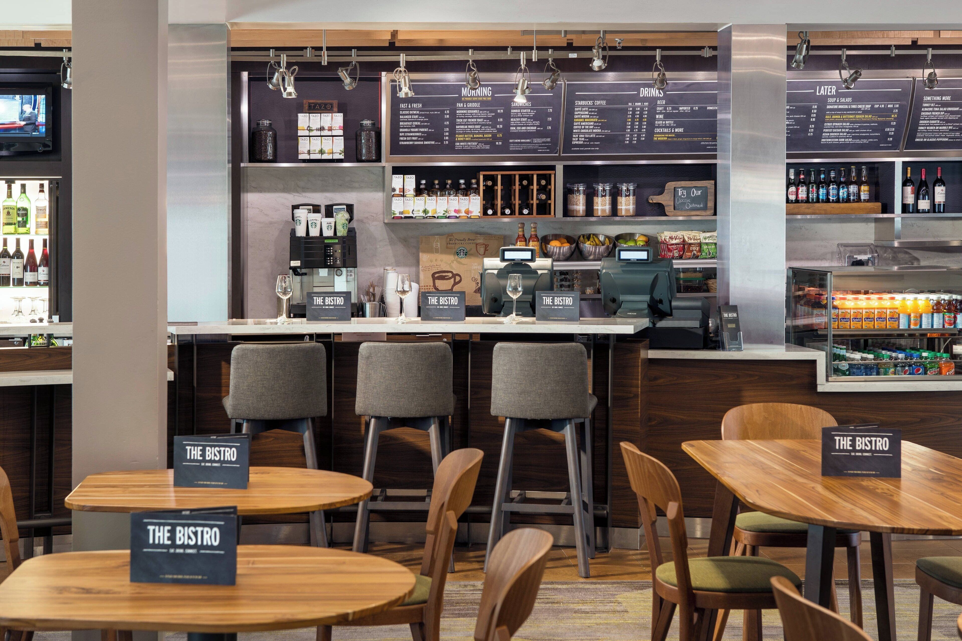 A modern bistro with wooden tables and chairs, a bar area, and a menu board displaying breakfast and drink options.