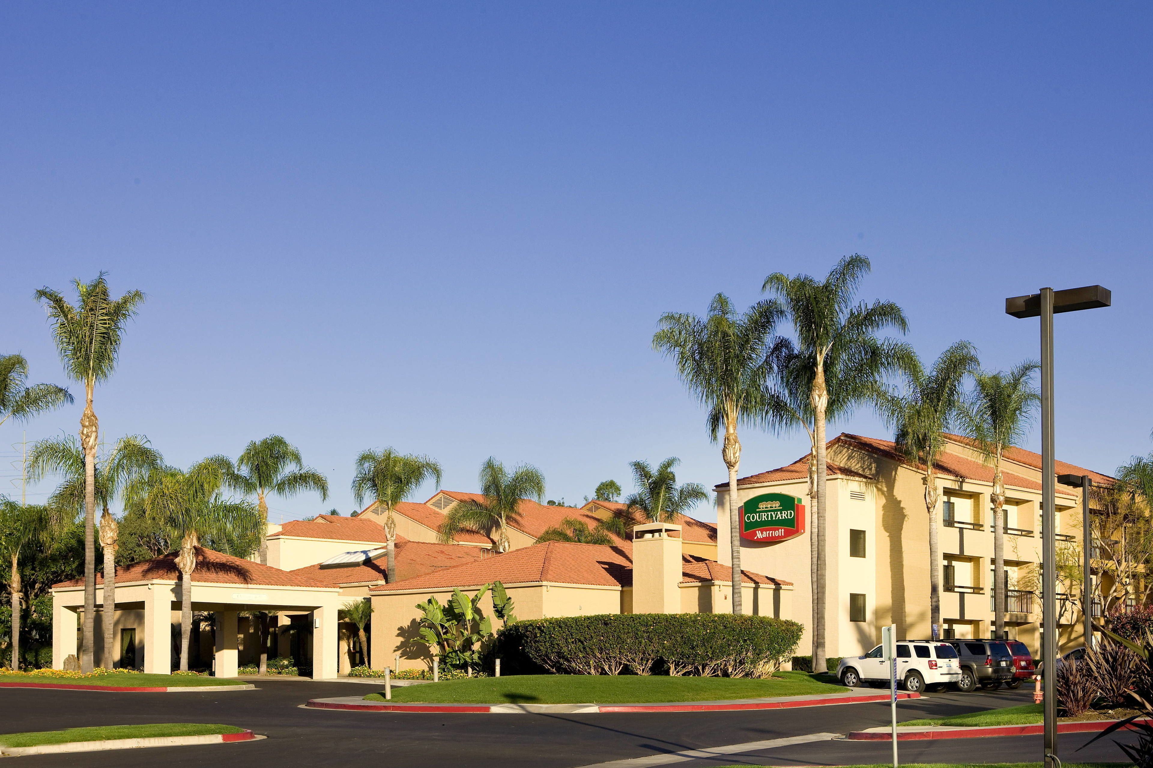 Un hotel Courtyard Marriott con entrada cubierta, palmeras y estacionamiento.
