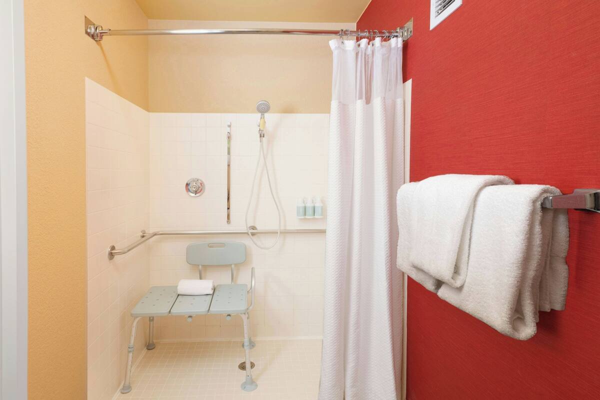 A bathroom with a shower, a grab bar, a wheelchair-accessible bench, and a towel rack.