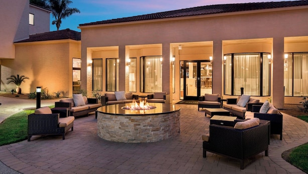 Un patio con un hogar circular rodeado de muebles de mimbre y una pared de piedra.