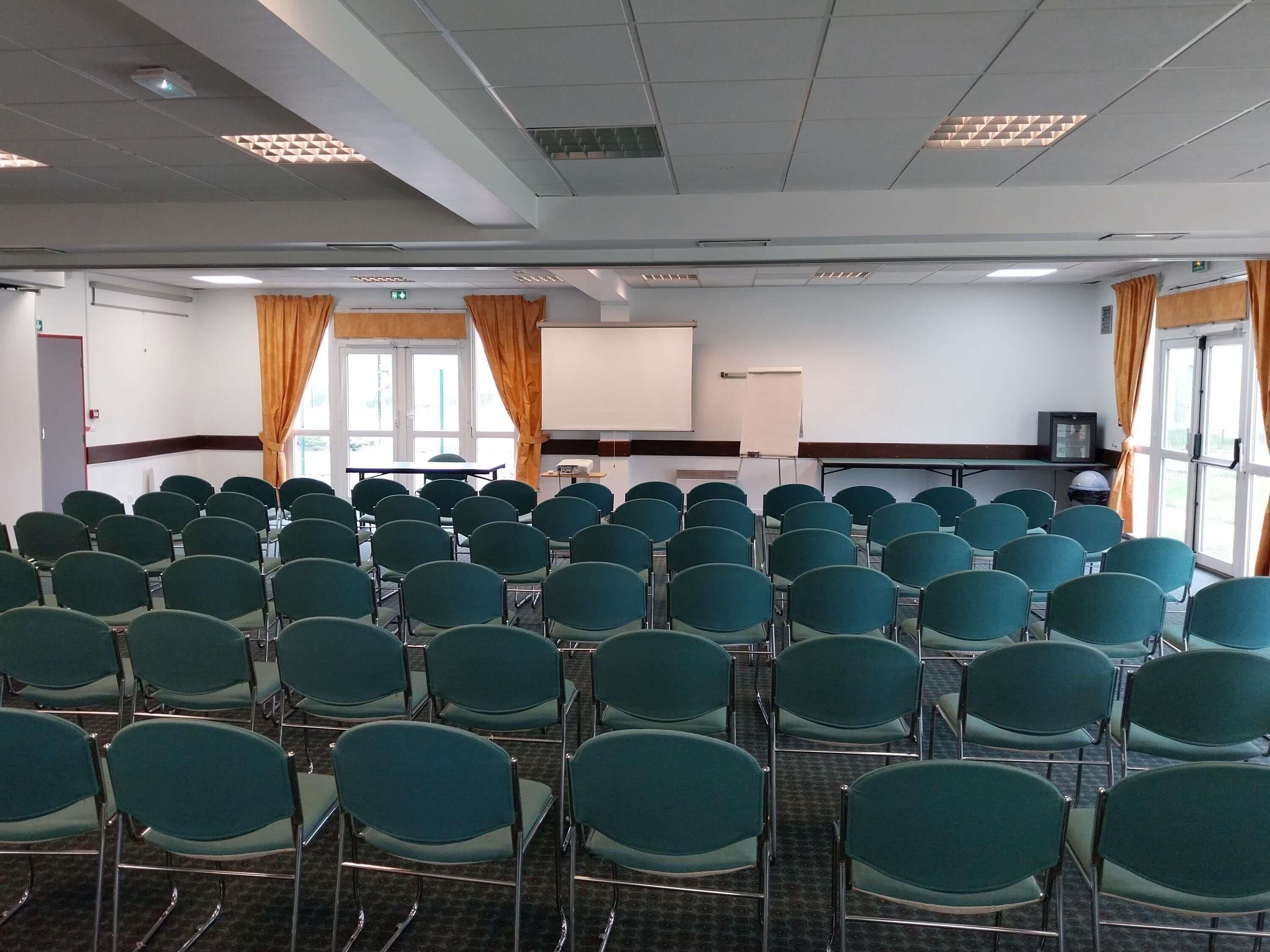 A conference room with rows of green chairs, a whiteboard, and a projector screen.