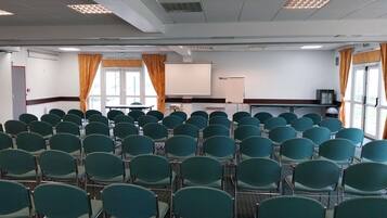 Uma sala de conferências com fileiras de cadeiras verdes, um quadro branco e uma tela de projeção.
