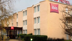 Un edificio de hotel con fachada color beige y múltiples ventanas. El nombre del hotel, "ibis", se muestra de forma destacada en el edificio y sobre la entrada.
