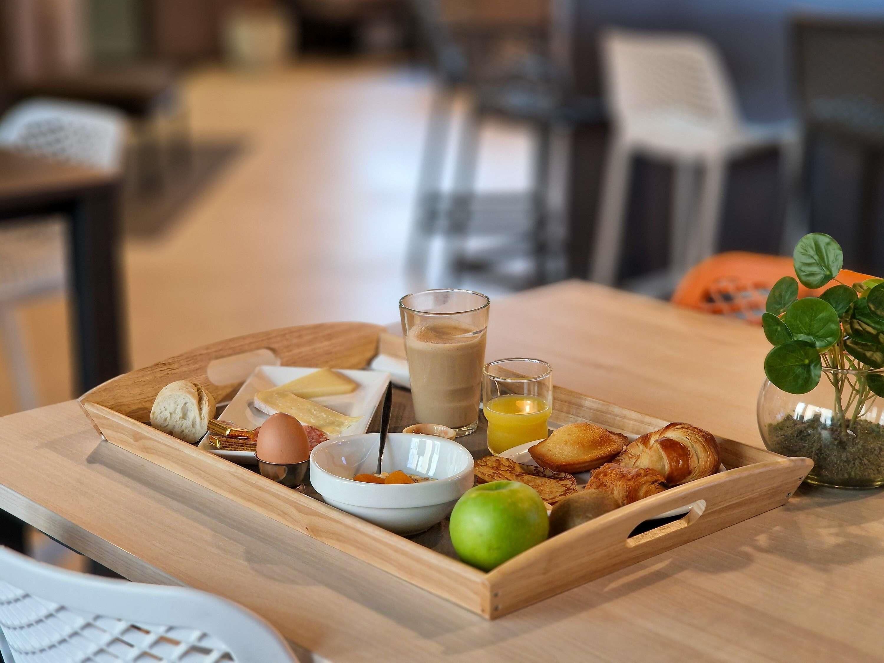 A wooden tray with breakfast items including croissants, a green apple, and a glass of coffee.