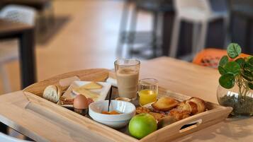 A wooden tray with breakfast items including croissants, a green apple, and a glass of coffee.