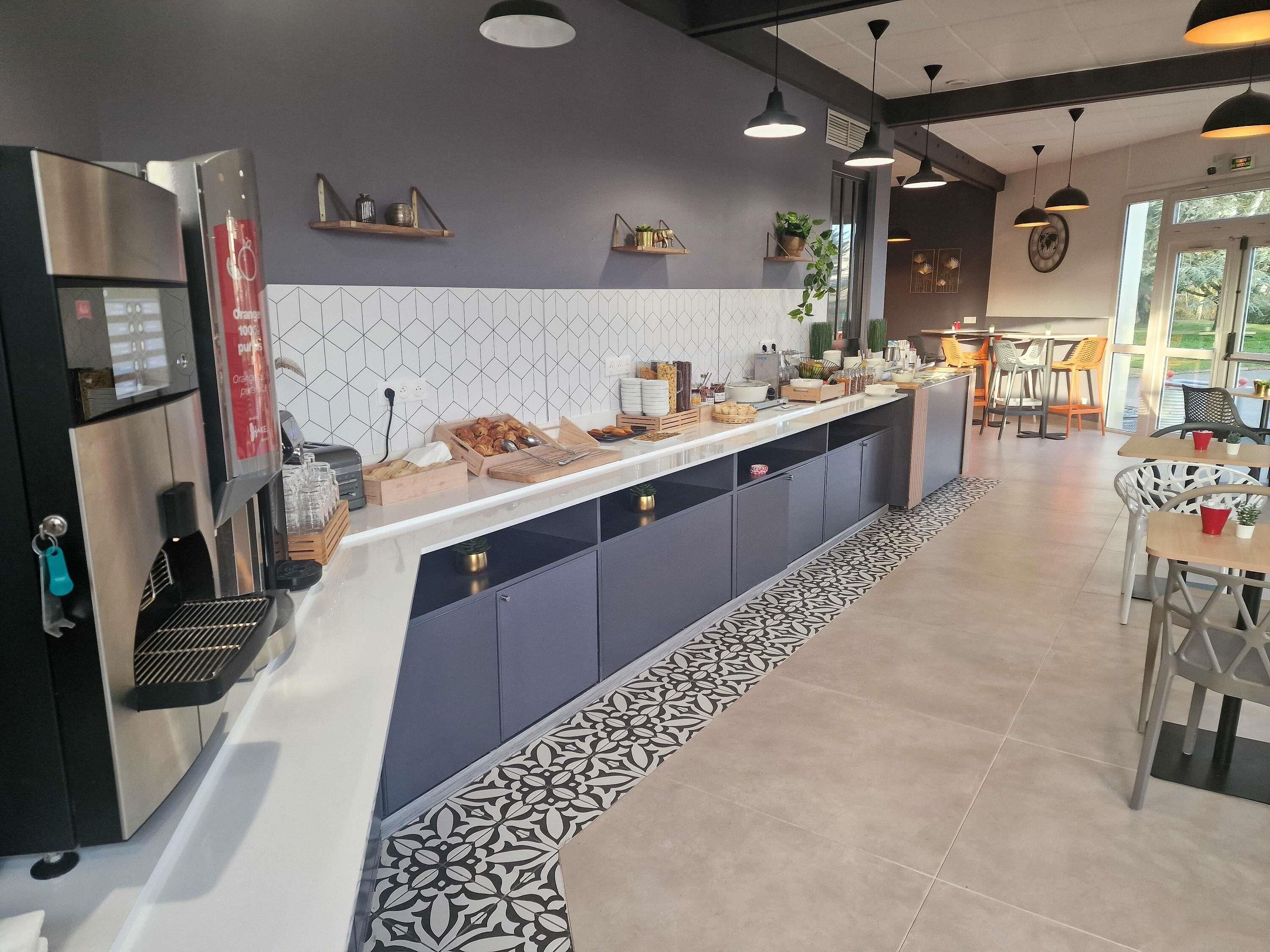 Une cuisine moderne équipée d’une machine à café intégrée, d’un comptoir où sont disposés des aliments et d’un espace repas avec des tables et des chaises.
