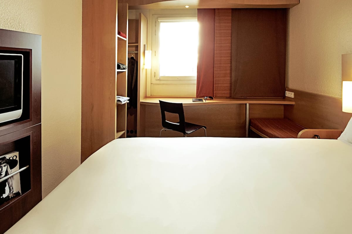 Una habitación de hotel con cama, escritorio, silla, televisor y armario.
