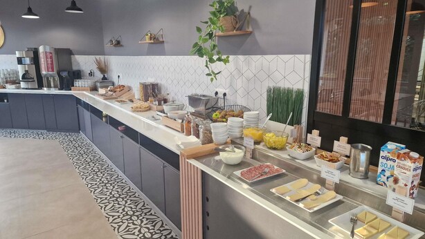Un bufé de desayuno con diversas opciones de comida, una máquina de café y una planta.